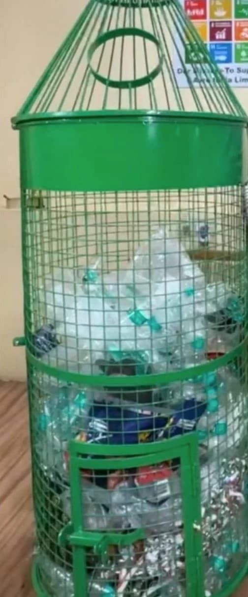 Reference photograph of the green bottle-shaped wire-mesh bin, filled with bottles and cans, standing indoors